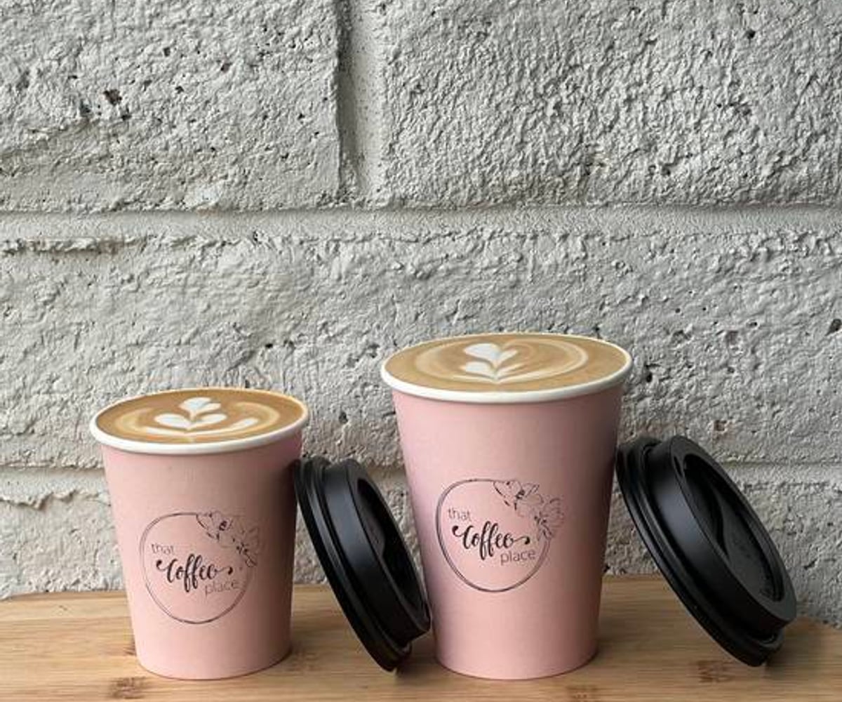 Two That Coffee Place takeaway cups on a timber bench