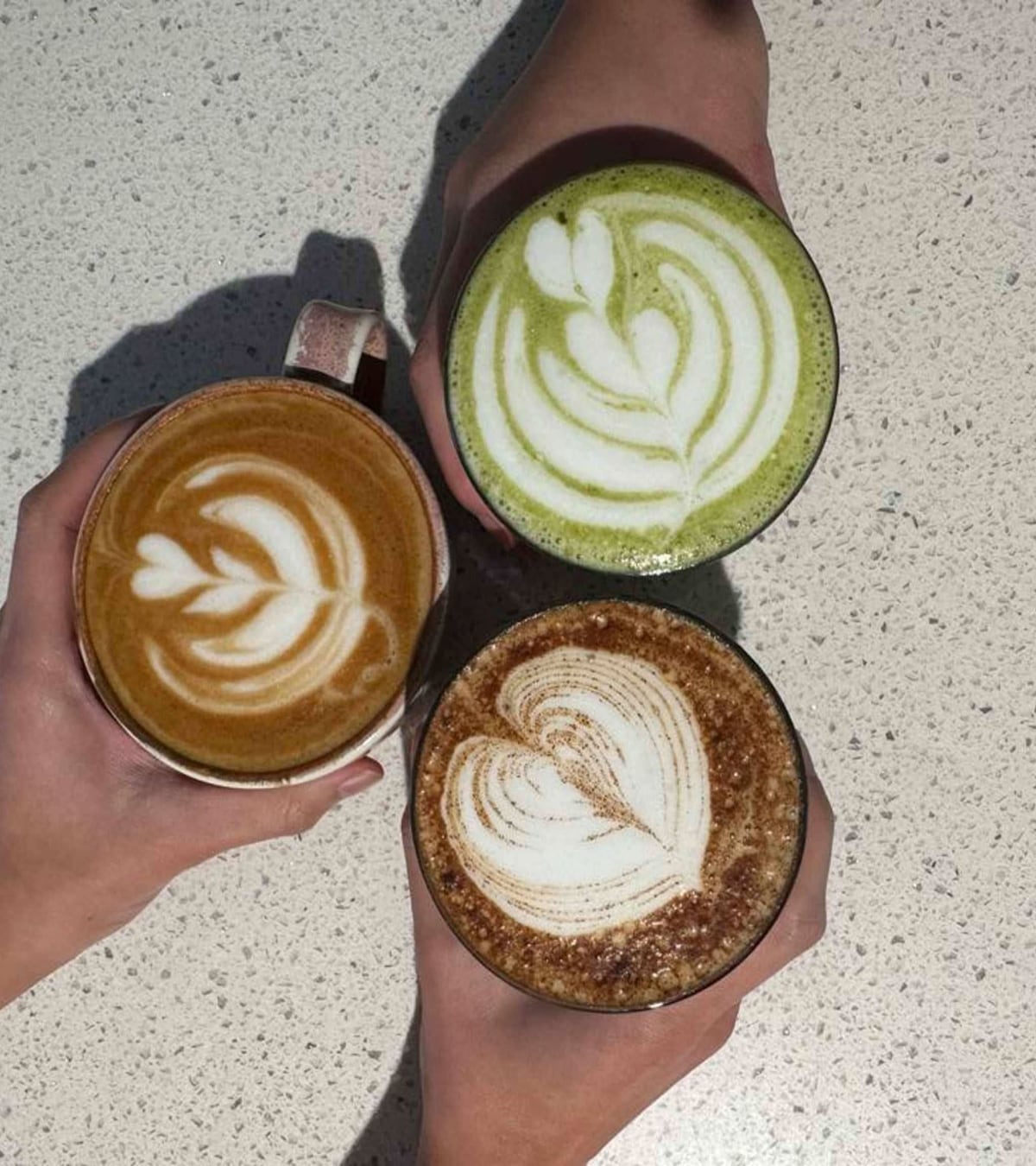 A latte, a matcha and a cappuccino held up in front of a bouquet at That Coffee Place