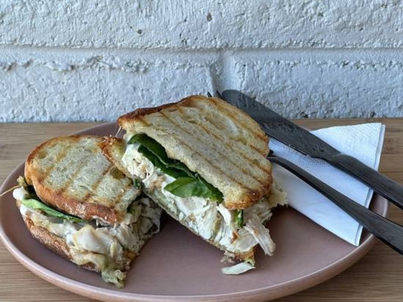 A toasted chicken pesto sandwich on a pink plate